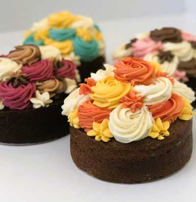 Three small chocolate cakes with colorful buttercream frosting on a white surface.