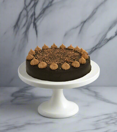 Chocolate cake with decorative elements on a white stand against a light background
